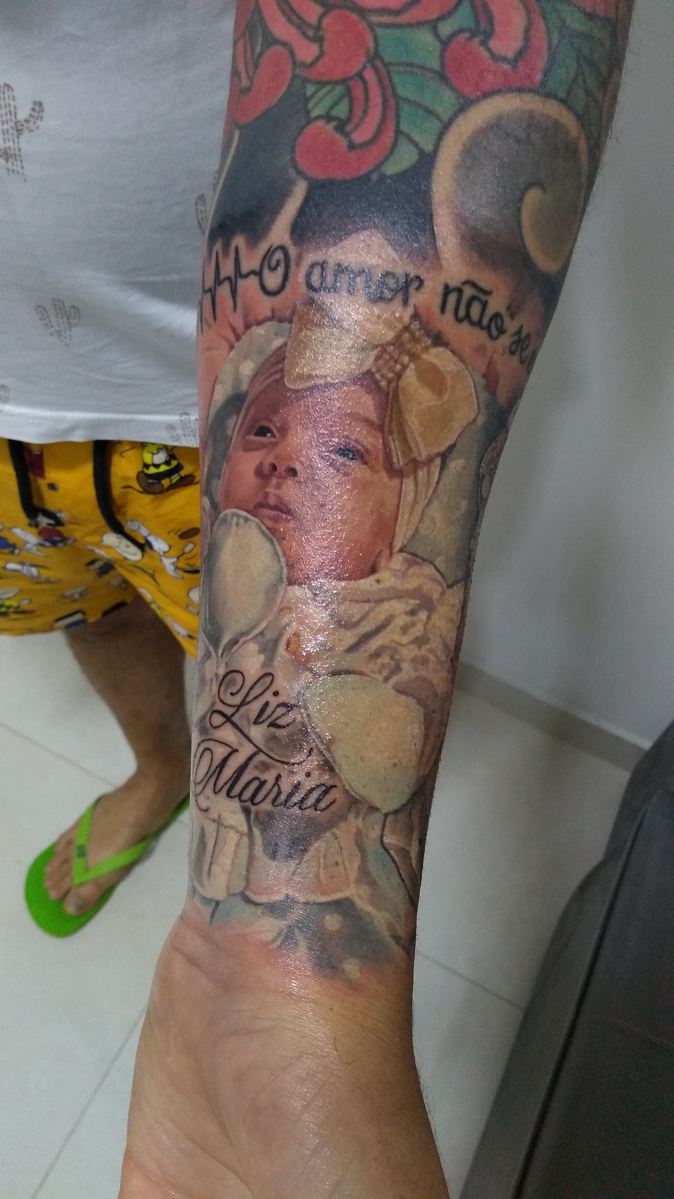 Retrato realista de Liz Maria no antebraço sem filtro polarizado — a mesma peça com reflexo da pele recém-tatuada